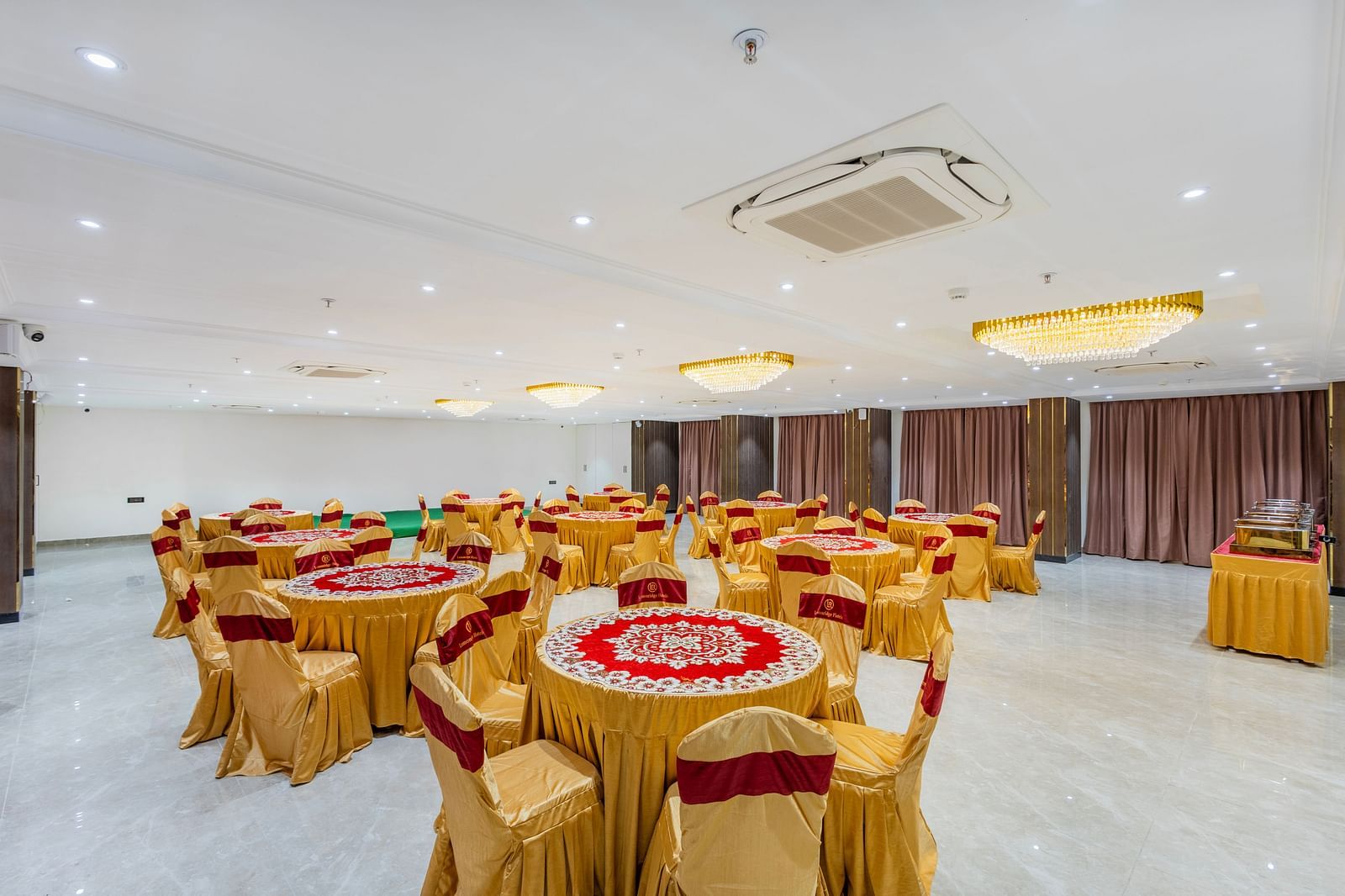 Lemonridge Hotels, KPHB | Banquet hall with round tables set for dining, featuring ornate chairs and centerpieces. Bright, spacious feel.